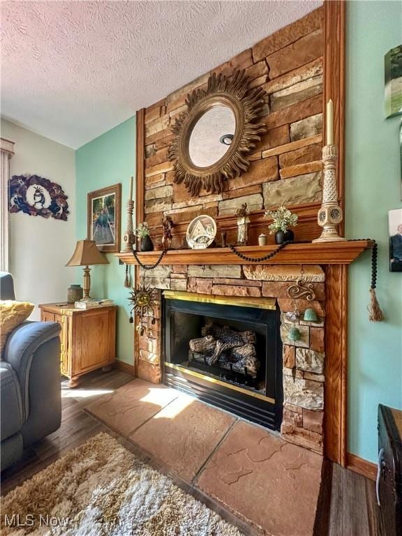 interior space with a textured ceiling, baseboards, a stone fireplace, and wood finished floors