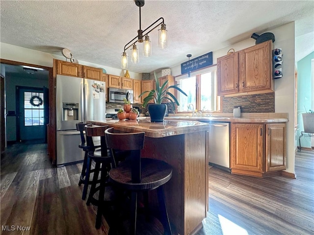 kitchen featuring decorative backsplash, dark wood-style flooring, a kitchen island, a textured ceiling, and stainless steel appliances
