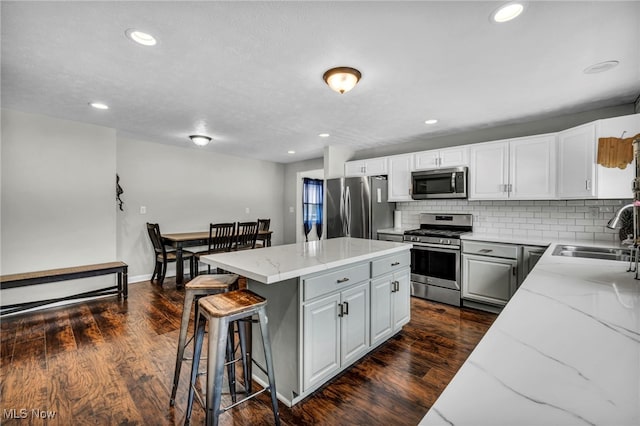 kitchen with a breakfast bar, a center island, light stone counters, a sink, and appliances with stainless steel finishes