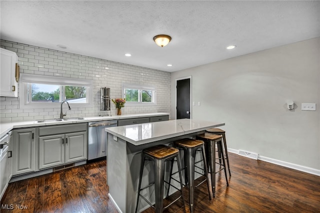 kitchen featuring visible vents, a kitchen bar, a sink, dishwasher, and gray cabinetry