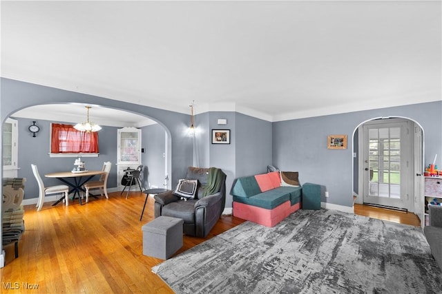 living area featuring arched walkways, baseboards, a notable chandelier, and wood finished floors