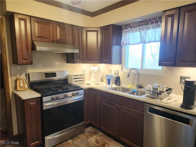 kitchen featuring light countertops, under cabinet range hood, a sink, stone finish flooring, and stainless steel appliances