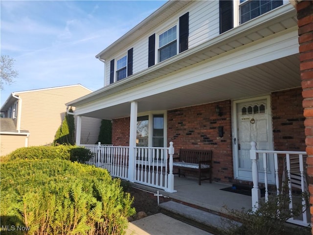 doorway to property featuring a porch and brick siding