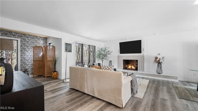 living area featuring baseboards, a lit fireplace, and wood finished floors