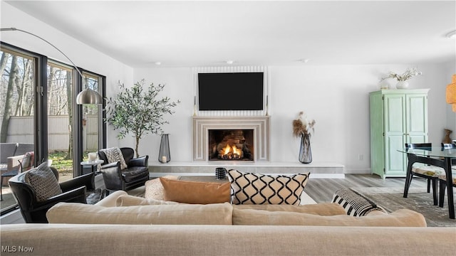living room featuring light wood-style floors, baseboards, and a lit fireplace