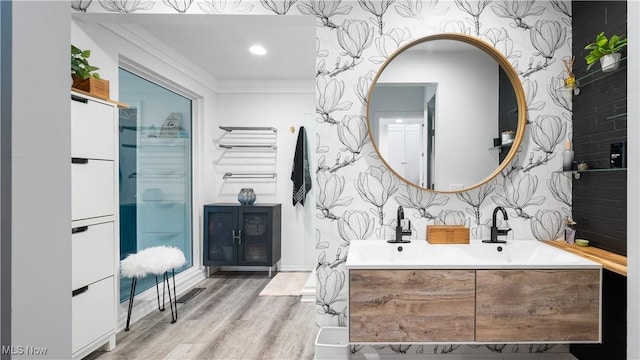 bathroom featuring double vanity, ornamental molding, wallpapered walls, and wood finished floors