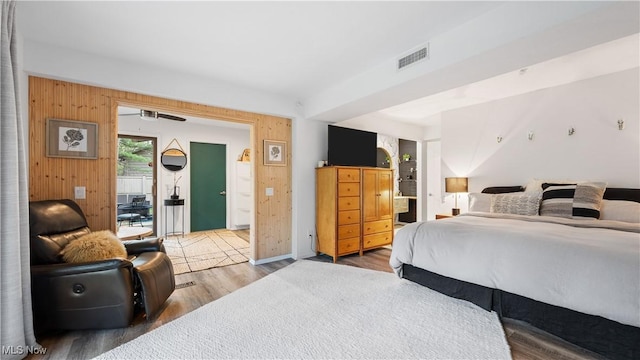 bedroom with baseboards, visible vents, wood walls, and wood finished floors
