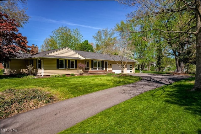 back of property featuring a garage, a yard, driveway, and a chimney