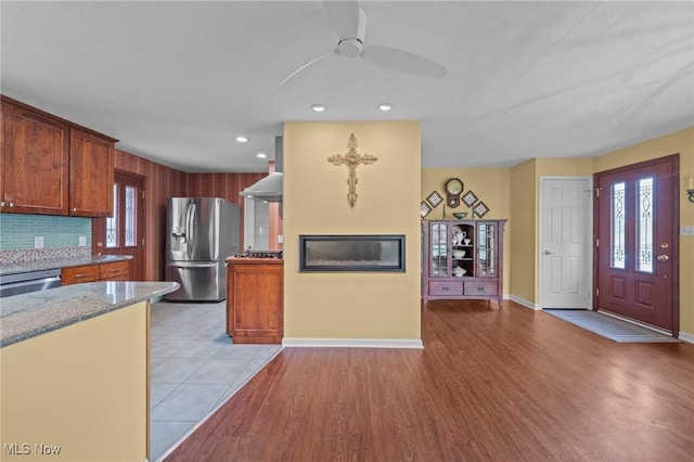 kitchen with stainless steel appliances, ceiling fan, light stone countertops, and a wealth of natural light