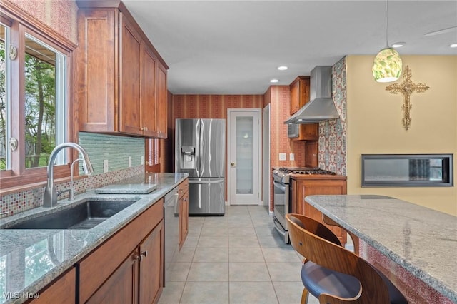 kitchen with wall chimney range hood, light stone counters, a sink, stainless steel appliances, and decorative backsplash