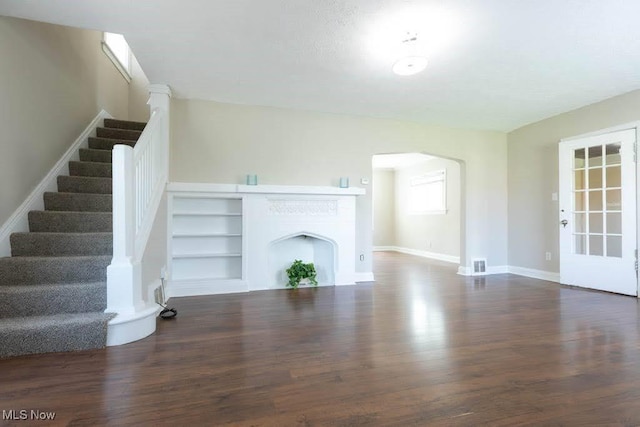 unfurnished living room featuring arched walkways, stairs, and wood finished floors