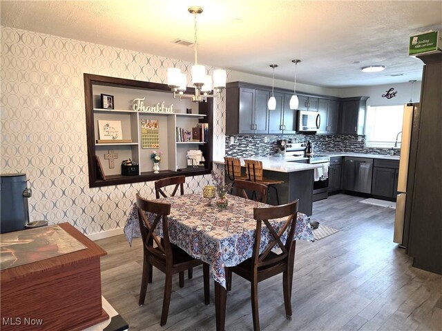 dining area featuring visible vents, baseboards, a chandelier, light wood-style floors, and wallpapered walls