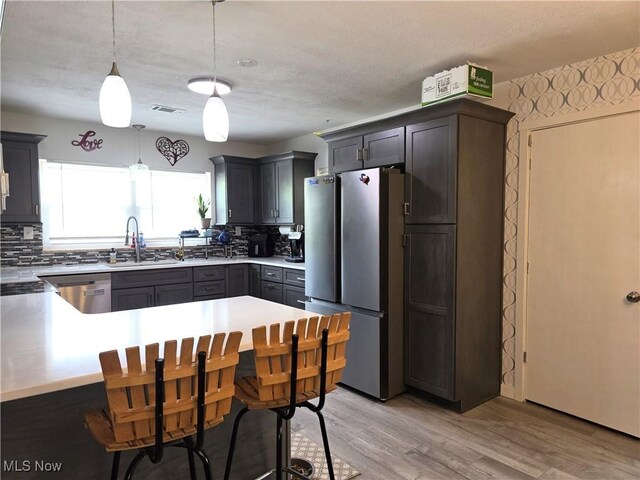 kitchen with a sink, appliances with stainless steel finishes, decorative backsplash, and light wood-style flooring