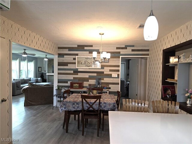 dining space with a textured ceiling, wallpapered walls, and wood finished floors