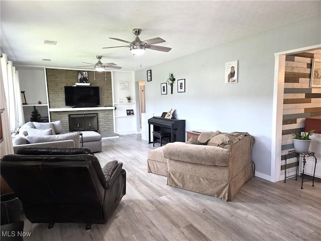 living area featuring a ceiling fan, visible vents, a fireplace, wood finished floors, and baseboards