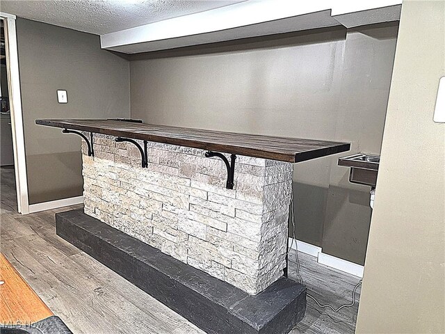 bar featuring baseboards, a textured ceiling, and wood finished floors