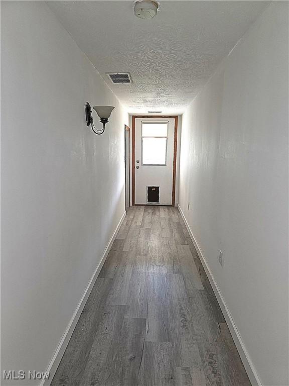 hall with a textured ceiling, baseboards, wood finished floors, and visible vents