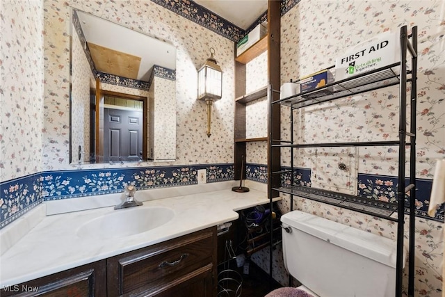 bathroom with toilet, wallpapered walls, and vanity