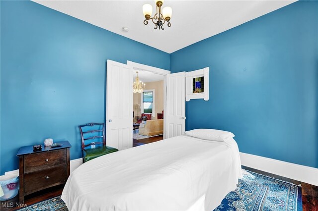 bedroom with baseboards, an inviting chandelier, and wood finished floors