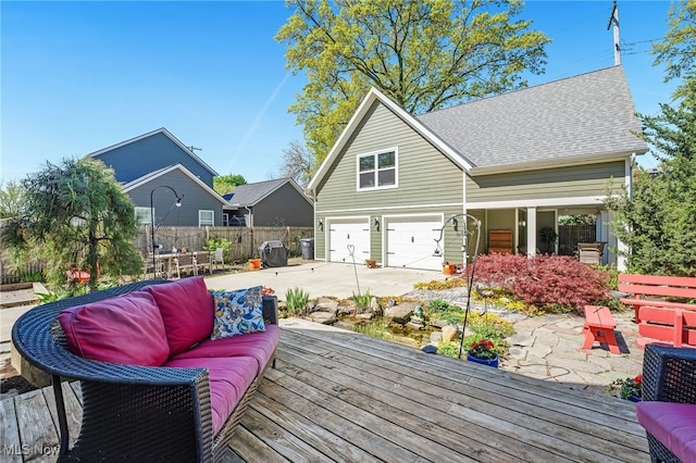 deck featuring a garage, outdoor lounge area, fence, and driveway