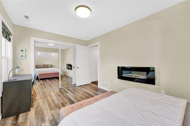 bedroom with baseboards, visible vents, wood finished floors, and a closet