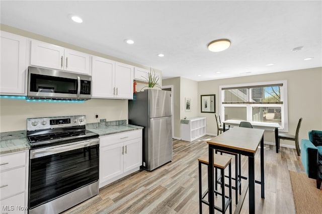 kitchen featuring stainless steel appliances, baseboards, white cabinetry, and light wood finished floors