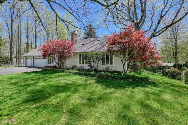 ranch-style home with an attached garage, a chimney, a front yard, and aphalt driveway