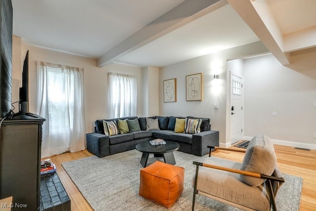 living area with baseboards, beamed ceiling, visible vents, and wood finished floors