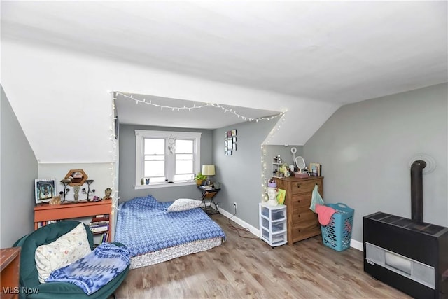 bedroom with baseboards, a wood stove, wood finished floors, and vaulted ceiling