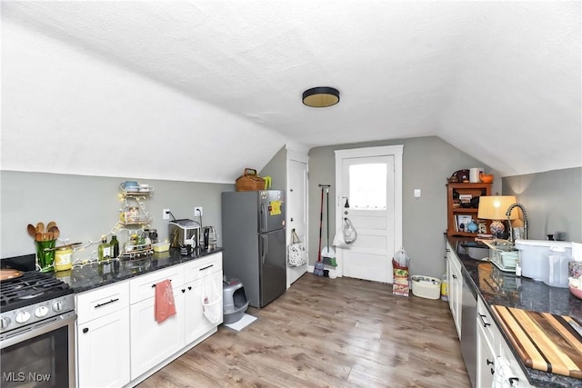 kitchen featuring white cabinets, stainless steel appliances, light wood-style flooring, and lofted ceiling