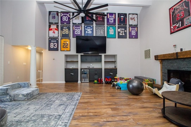 interior space with a high ceiling, ceiling fan, wood finished floors, ornate columns, and visible vents