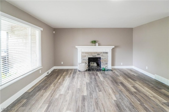 unfurnished living room with baseboards, visible vents, a stone fireplace, and wood finished floors