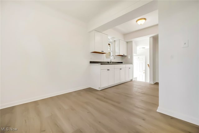 kitchen with white cabinets, baseboards, a sink, and light wood finished floors
