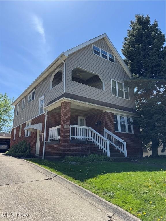 view of front of home with covered porch, a front lawn, and brick siding