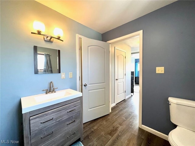 bathroom with toilet, baseboards, wood finished floors, and vanity