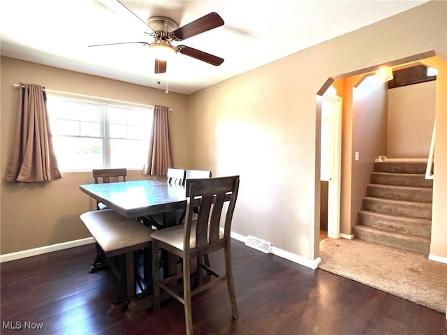 dining space featuring arched walkways, dark wood finished floors, stairs, a ceiling fan, and baseboards