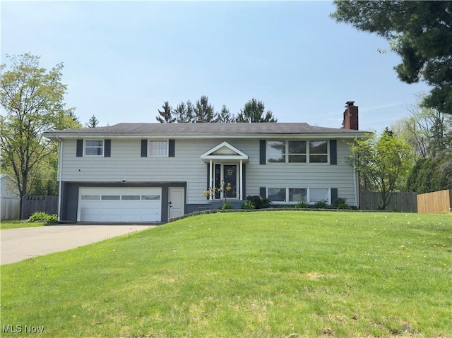 bi-level home featuring fence, a chimney, an attached garage, and a front lawn