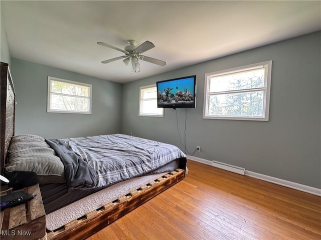 bedroom featuring wood-type flooring, a ceiling fan, baseboards, and a baseboard heating unit