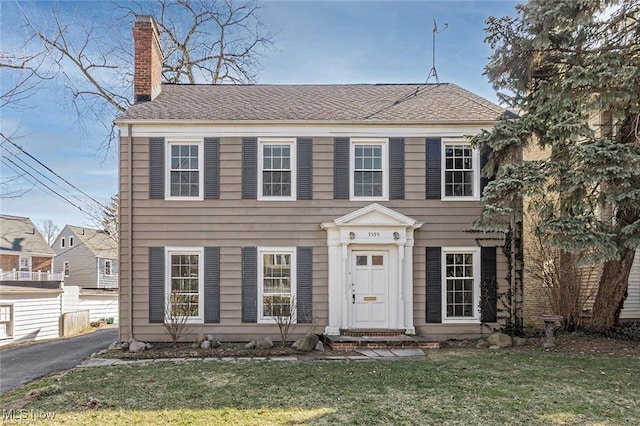 colonial-style house with a chimney and a front yard