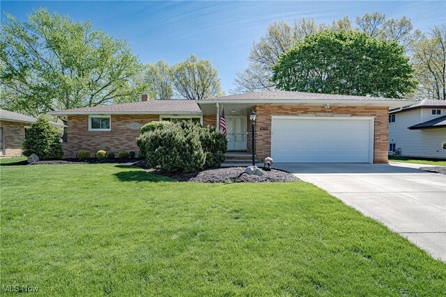 ranch-style house featuring a chimney, a front yard, brick siding, concrete driveway, and an attached garage