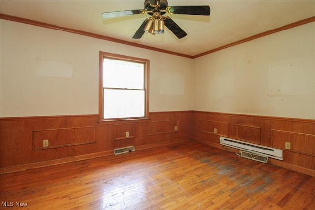 unfurnished room featuring visible vents, wood-type flooring, a wainscoted wall, a ceiling fan, and a baseboard heating unit
