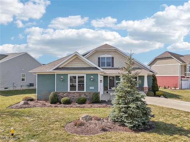 craftsman house with a shingled roof, stone siding, and a front yard