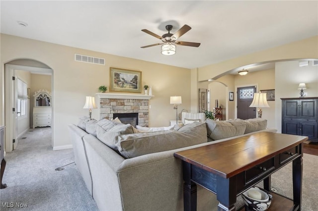 living area with light colored carpet, arched walkways, a stone fireplace, a ceiling fan, and visible vents