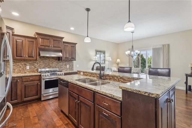 kitchen with a sink, stainless steel appliances, decorative backsplash, under cabinet range hood, and dark wood-style floors
