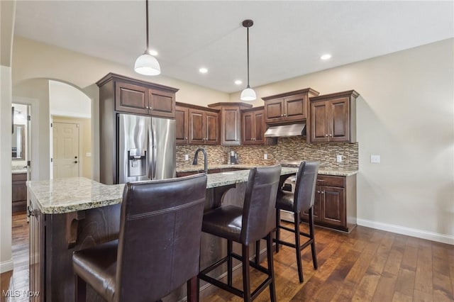 kitchen featuring stainless steel fridge, decorative backsplash, arched walkways, and under cabinet range hood