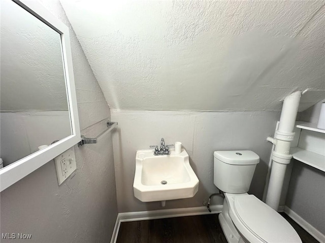 half bath featuring lofted ceiling, wood finished floors, toilet, baseboards, and a sink