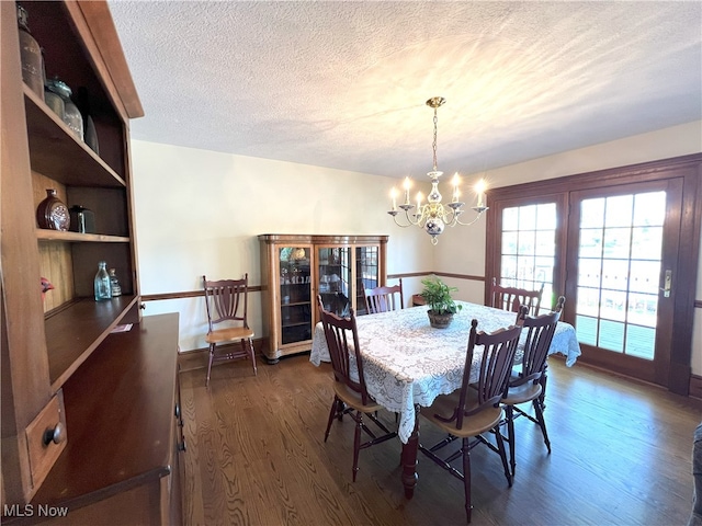 dining space with dark wood-style flooring, a textured ceiling, and a notable chandelier