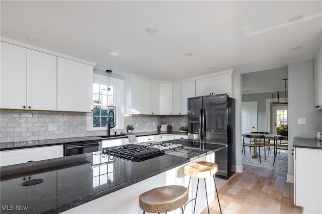 kitchen with a kitchen breakfast bar, tasteful backsplash, white cabinetry, black appliances, and light wood-style flooring