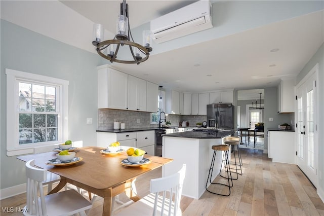 kitchen with plenty of natural light, dark countertops, a wall mounted air conditioner, refrigerator with ice dispenser, and a notable chandelier