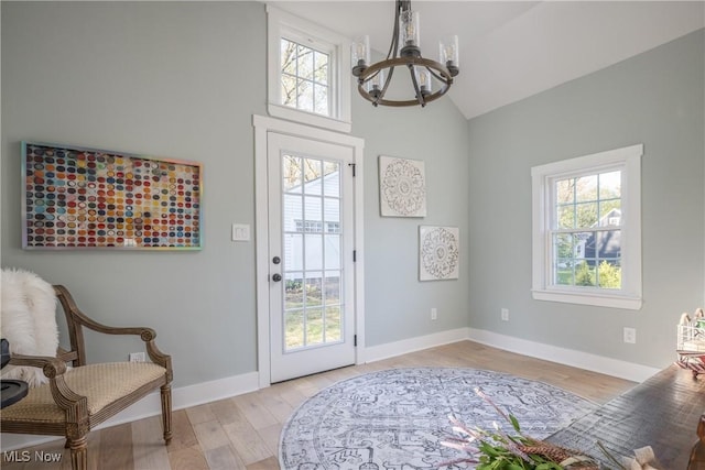 doorway with an inviting chandelier, light wood-style floors, plenty of natural light, and high vaulted ceiling